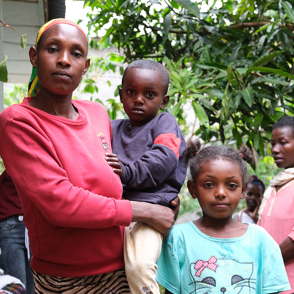 a widow in a red sweater carries her young son and stands beside her daughter, who is approximately eight years old