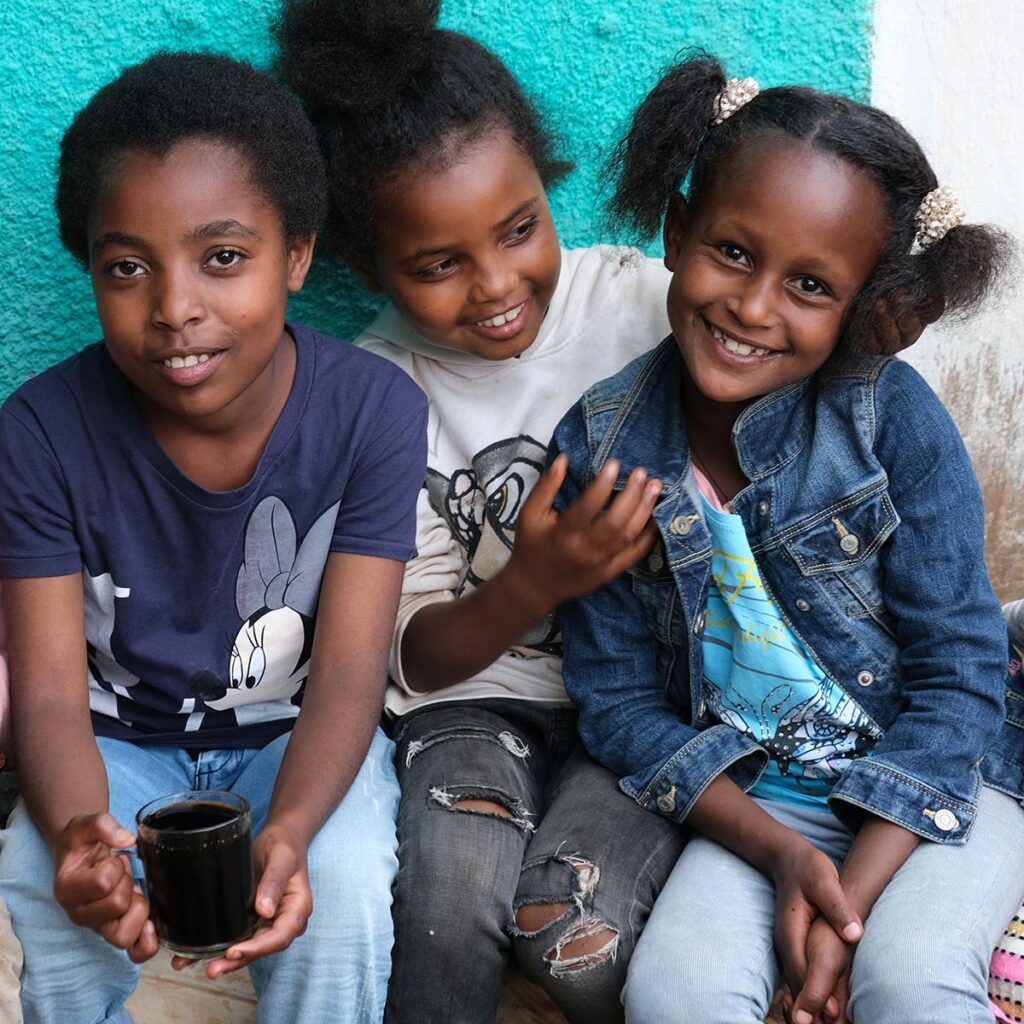 two girls smiling and laughing together sitting next to a boy smiling cautiously at the camera